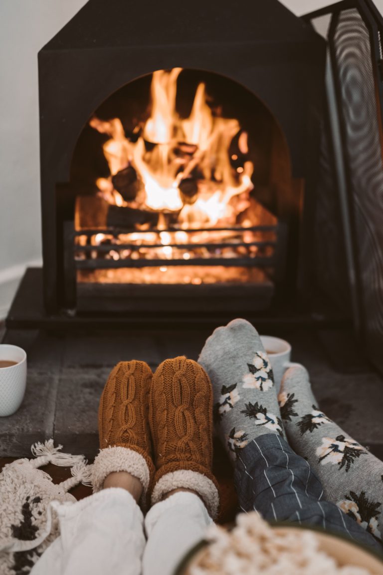 Two people wearing socks warming their feet in front of the fire