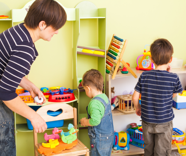 A woman in a striped shirt is in a play room with two children. There are a number of bright and colourful toys surrounding them